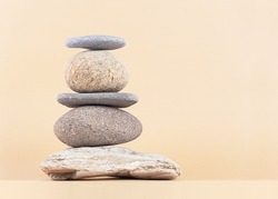 Stack of rocks on a beige background. Balancing pyramid of five sea stones, front view, copy space. Harmony, balance, spa therapy, zen concept.