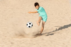 Beach soccer on sand. Boy soccer player kick ball trying to score goal in football match. Sports and recreation for children during summer holidays