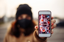 Girl shows a mobile phone with coronavirus sign. Young woman in city street wearing black sterile medical face mask. Quarantine COVID-19 pandemic coronavirus epidemic and health care concept