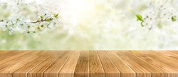 Spring background with white blossoms and sunlights in front of a wooden table. Spring apple garden on the background.