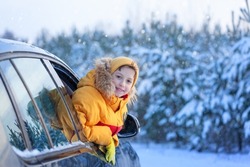 Winter holiday. Boy child is leaning out of the car window and enjoying snow road and forest winter. Happy kid travel with family on the car.