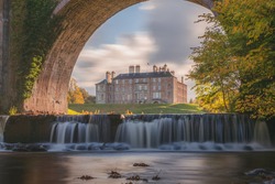 Dalkeith Country Park with waterfall and arch framing manor house on a sunny autumn afternoon makes for an ideal day trip from Edinburgh in Scotland.