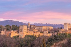 Classic view with pink sunset or sunrise sky of Charles V Palace, the iconic Alhambra and Sierra Nevada Mountains from Mirador de San Nicolas in the albaicin old town of Granada, Andalusia, Spain.