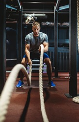 Happy fit men with battle ropes exercise in the fitness gym