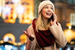 Portrait of young smiling beautiful woman using smartphone on the street at winter