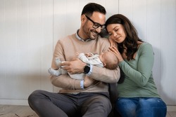 Portrait of young happy man and woman holding newborn cute babe dressed in white unisex clothing.