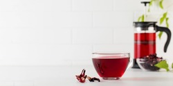 Herbal tea made from hibiscus petals in a transparent cup on a light background, teapot and a bowl of dry hibiscus.