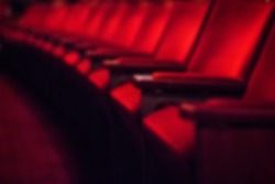 Blurred dark background: row of empty red theater chairs