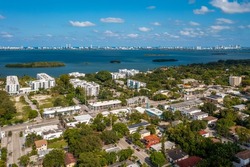 Aerial shot of Upper East Side residential neighborhood
in Miami, lush vegetation is seen, modern buildings, luxury houses, urban skyline, blue sky, street with cars