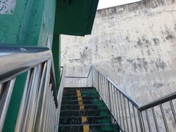 Street photo of a green overpass stairway with steel railings. For people crossing the road in Thailand. There is a large cement wall as a background, suitable for graffiti.