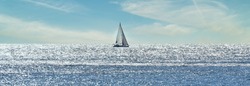 Small sailboat sailing through a silver sea in a sunny day 