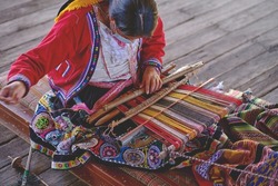 Indigenous woman showing traditional weaving technique and textile making in the Andes mountain range of South America in Peru, Selective focus.