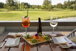 Gourmet food. Elegant sushi restaurant. Outside table set up and dish presentation. Raw salmon sushi plate with white wine and drink, with a beautiful golf course and lake view in the background. 