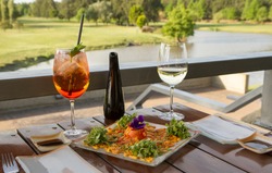 Gourmet food. Elegant sushi restaurant. Outside table set up and dish presentation. Raw salmon sushi plate with white wine and drink, with a beautiful golf course and lake view in the background.