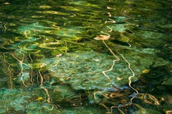 Natural texture. Jungle natural pond. Closeup view of the emerald color water cenote with rocks in the bed. The transparent water surface reflects sunlight. 