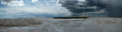 Natural resources. Industry. Panorama view of the white salt flats and open cast mining pit under a dramatic sky.