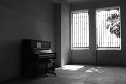 Piano in an empty room, there are bars in the windows. In black and white.