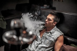 Young man blowing clouds of smoke in the hookah bar.