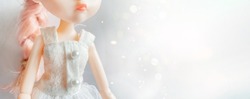 A doll in a white dress with pink hair stands against a magical bokeh background. 