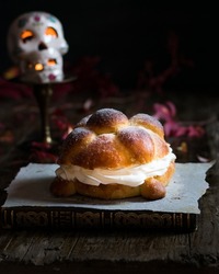 Dead bread stuffed with whipped cream on wood with black background and skull