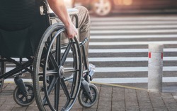 Disabled man on wheelchair preparing to cross the road on pedestrian crossing, copy space.