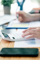 Cropped image of woman hand using calculator, working with graph chart and analyzing business strategy, financial statistic, sitting at desk office, vertical view.