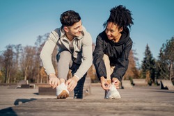 A man and a woman adjust their shoes on the street, take a break. Outdoor sports activities. A couple in love together. Training in a park in the city center. Healthy lifestyle