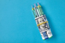 Insulin syringe pens wrapped in dollar bills on a blue background