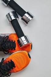 Metal dumbbell fell on the feet of an athlete in orange sneakers. Safety precautions when training with heavy equipment. Top view with copy space