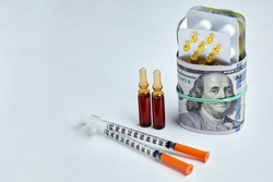 Pills, ampoules and syringes are wrapped in dollar bills, fastened with an elastic band on a white background. Rising drug prices and pharmaceutical monopoly profits