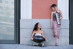Two street musicians looking each other and laughing, playing instruments.