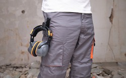Unrecognizable builder with hearing protection hanging from the trousers. Safety at work concept.