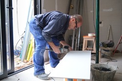Senior constructor worker cutting a white ceramic tile with a radial saw.