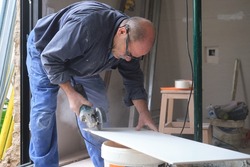 Professional tiler cutting a white ceramic tile with a radial saw.