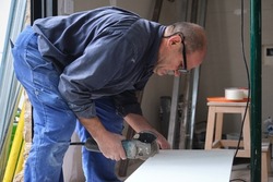 Senior contractor worker cutting a white ceramic tile with a radial saw.