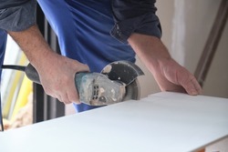 Unrecognizable mason cutting a white ceramic tile with a radial saw.