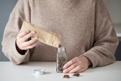 Unrecognizable woman refilling spice jar with star anise from paper bag buyed at package free grocery store.