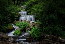 Long exposure shot with silky water fall , river flowing through the forest with mountain surrounding. Uttarakhand India.