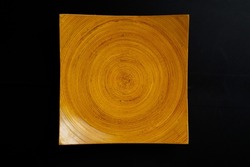 square wooden plate with concentric circles pattern. Orange textured dish isolated on black background. 