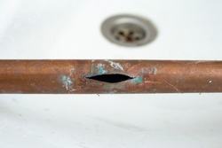 Cracked open copper pipe due to freezing with water inside, close up