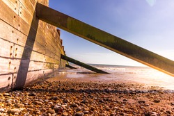 Wooden sea defence wall with stones and pebbles on the beach at Camber Sands in England on a summers day