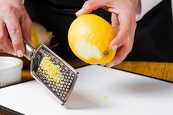 Close-up of housewife in black apron grating natural lemon