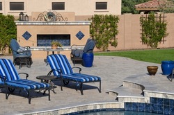 A desert landscaped backyard in Arizona featuring a travertine tiled pool deck and artificial grass.
