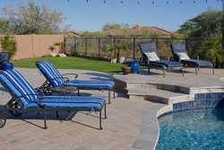 A desert landscaped backyard in Arizona featuring a travertine tiled pool deck and artificial grass.