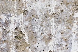 An old concrete wall with remnants of gray paint crumbling from time. Texture of eroded concrete.