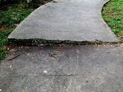 The path of the pedestal is damaged by the roots of the tree below which grows to cause the cement path to be uneven.