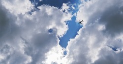 The passenger airplane is flying far away in blue sky and clouds. Dramatic clouds with the sun shining through them. Aircraft in the air. Horizontal stories. International passenger air transportation