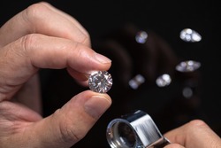 Round shape diamond in hands of jeweller. Man jeweller examines a diamond. Gem grading and checking. Diamond business.