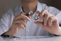Round cut diamond in hand of diamond expert estimating quality of large gem stone through magnifying glass.