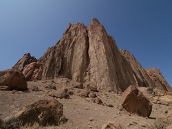 Close up of Shiprock Mountain from the base with large boulders scattered in the foreground and deep blue sky above.